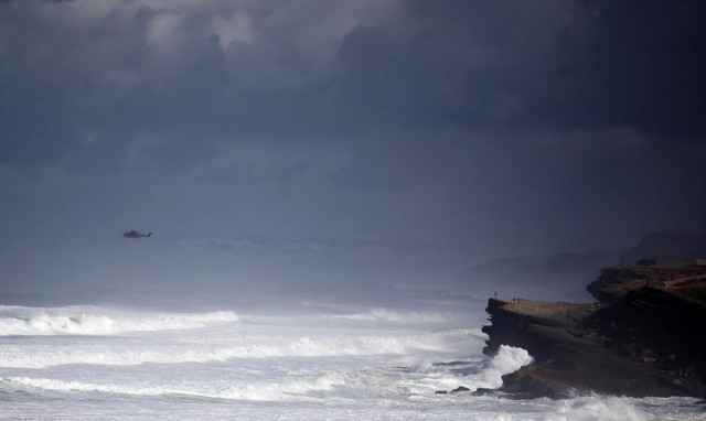 Mọi người nhìn ra biển trong khi trực thăng cứu hộ đang tìm kiếm 5 ngư dân mất tích ở bãi biển Macas, gần Sintra, Bồ Đào Nha.