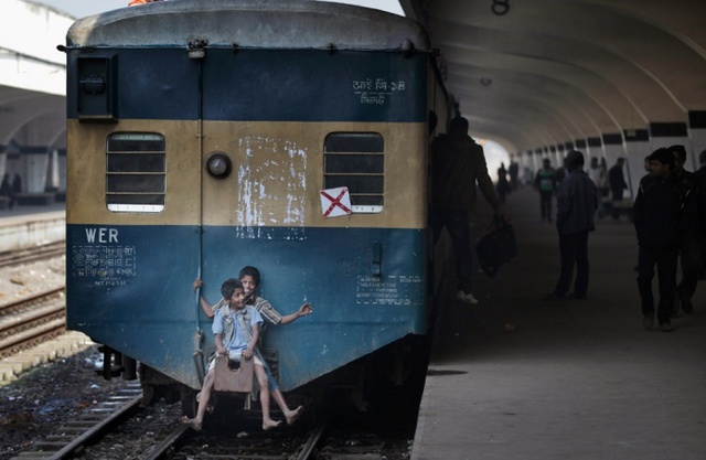Trẻ em ngồi sau đoàn đang chạy tại một nhà ga tàu hỏa ở  Dhaka, Bangladesh.