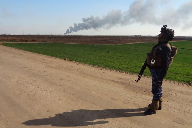 Thành viên của lực lượng an ninh Iraq đứng trên đường khi cột khói bốc lên từ nhà máy khai thác dầu bỏ Khubbaz ở phía tây thành phố Kirkuk.