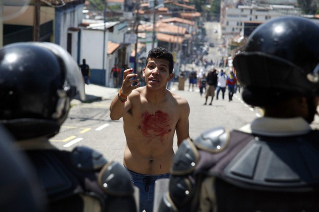Một thanh niên biểu tình trước mặt cảnh sát sau khi học sinh Kliever Roa 14 tuổi thiệt mạng trong một cuộc đụng độ với cảnh sát tại thành phố San Cristóbal, Venezuela.
