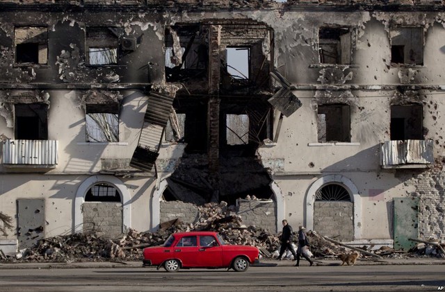 Người dân đi bộ qua một tòa nhà bị hư hại trong các cuộc giao tranh ở Vuhlehirsk, phía nam của Debaltseve, Ukraine.