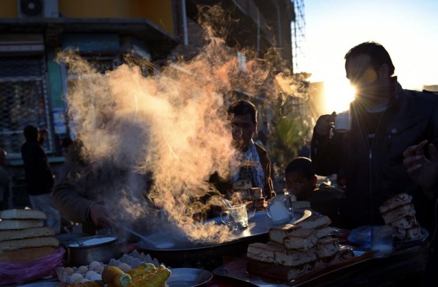 Khách hàng uống sữa nóng và ăn sáng với bánh tại một gian hàng bên đường ở Kabul, Afghanistan.