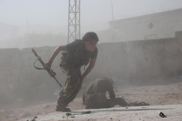 Một chiến binh phiến quân Syria chạy tới giúp đỡ một chiến hữu bị thương trong cuộc giao tranh với quân đội chính phủ ở tỉnh Idlib.