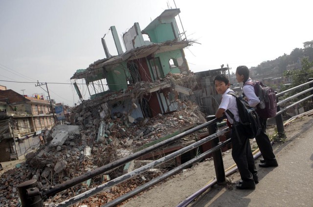 Học sinh đứng chờ xe bus trước những ngôi nhà bị phá hủy do động đất ở Kathmandu, Nepal.