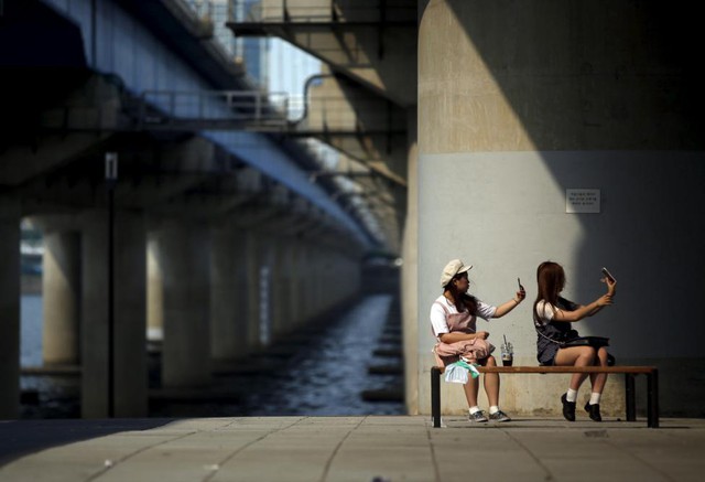 Hai cô gái chụp ảnh “tự sướng” khi họ ngồi nghỉ ngơi dưới một cây cầu trong công viên sông Hàn ở Seoul, Hàn Quốc.
