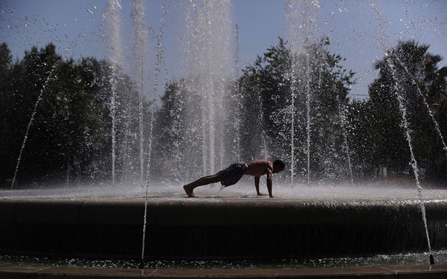 Người đàn ông thể dục chống đẩy trên đài phun nước trong một ngày nắng nóng ở Seville, Tây Ban Nha.
