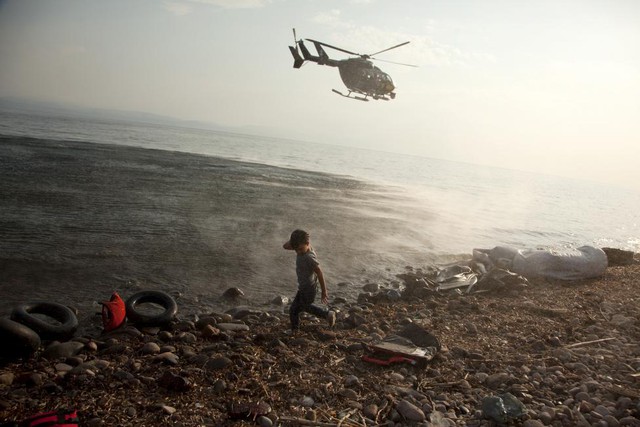 Máy bay trực thăng Frontex tuần tra trên đầu một cậu bé tị nạn người Syria vừa cập bến vào bãi biển trên đảo Lesbos, Hi Lạp.