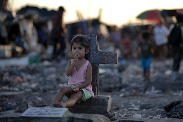 Bé gái ngồi cạnh bia mộ tại khu ổ chuột nằm trong nghĩa trang thành phố Navotas, Philippines.