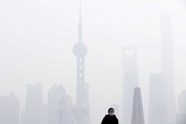 Người phụ nữ đeo khẩu trang đứng trên cây cầu trong bầu không khí ô nhiễm trước trung tâm tài chính Phố Đông ở Thượng Hải, Trung Quốc.