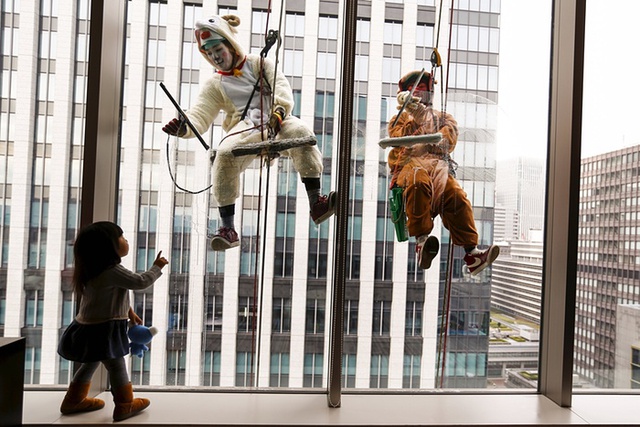 
Bé gái nhìn công nhân lau cửa kính hóa trang thành cừu và khỉ trên một tòa nhà cao tầng ở Tokyo, Nhật Bản.
