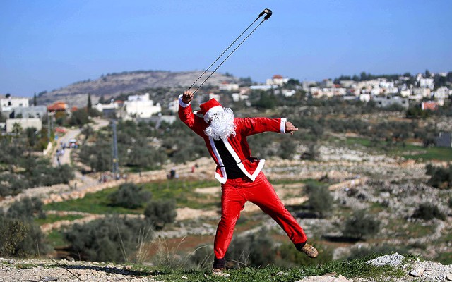 Người biểu tình Palestine mặc trang phục ông già Noel, quăng đá vào lực lượng an ninh Israel trong cuộc đụng độ tại khu định cư của người Do Thái ở ngôi làng Bilin, Bờ Tây.