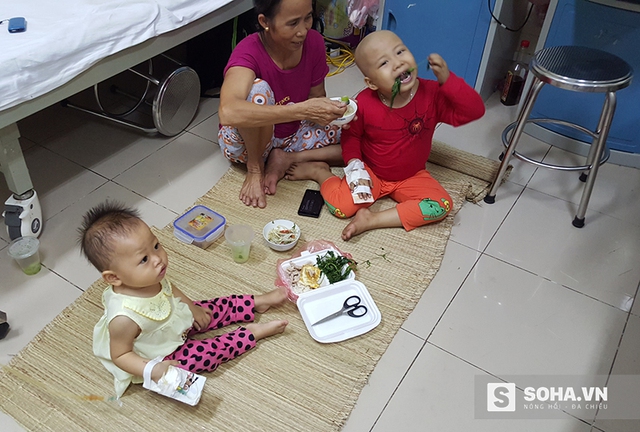 
Hai em bé bị K đang được người thân cho ăn tối tại lối đi giữa 2 giường bệnh.
