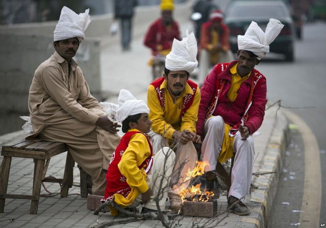 Những nghệ sĩ đường phố ngồi sưởi ấm quanh đống lửa trong khi chờ người xem ở thành phố Rawalpindi, Pakistan.