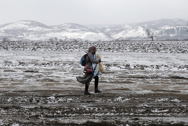 Người phụ bế con nhỏ đi trên cánh đồng phủ đầy băng tuyết trong hành trình di cư từ Macedonia sang Miratovac, Serbia.