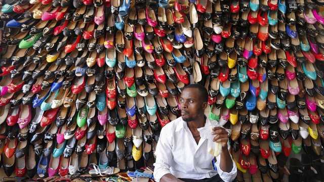 Chủ cửa hàng ngồi trước hàng trăm đôi giày đủ màu sắc được treo trên tường ở Kampala, Uganda.
