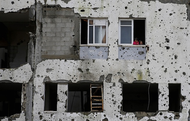 Những đứa trẻ Palestine nhìn ra từ một ô cửa sổ của khối căn hộ đã bị hư hại nặng nề trong cuộc chiến giữa Israel và Hamas năm 2014.