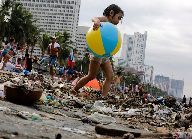 Bé gái ôm bóng đi qua bãi biển ngập rác thải tại Manila Bay, Philippines.