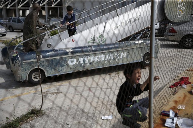 Cậu bé di cư ngồi khóc cạnh hàng rào bên ngoài tòa nhà cũ ở thành phố Athens, Hi Lạp.