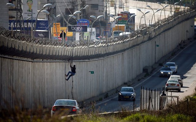 Người đàn ông Palestine dùng dây để trèo qua bức tường do Israel xây dựng để chia đôi thành phố Al-Ram, Bờ Tây.