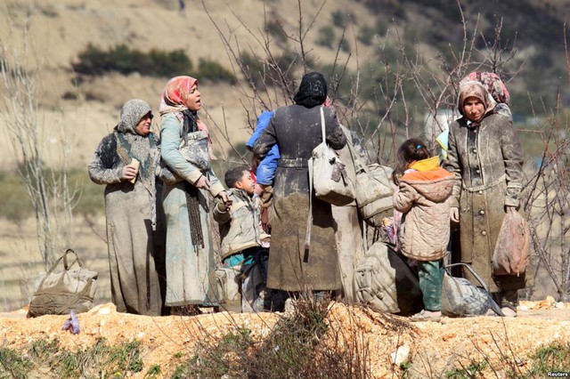 Những người di cư mặc quần áo dính đầy bùn đất đứng chờ để vượt qua biên giới sang Thổ Nhĩ Kỳ từ thị trấn Khirbet Al-Joz, Syria.