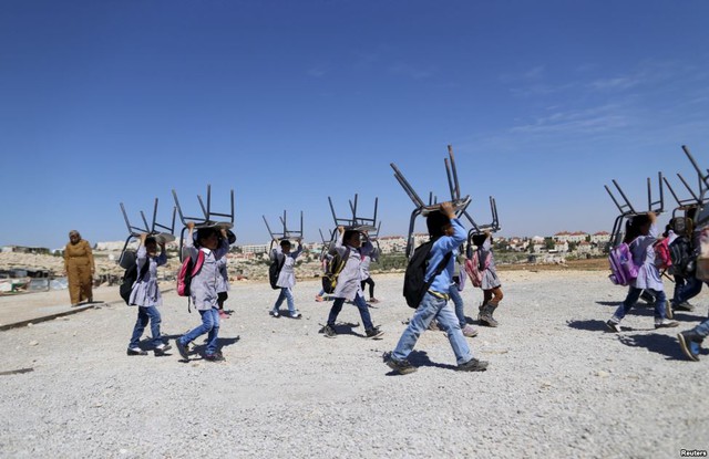 Trẻ em người Palestine đội ghế trên đầu trên đường về nơi ở sau khi tham dự một lớp học ngoài trời tại ngôi làng Al-Eizariya, Bờ Tây.