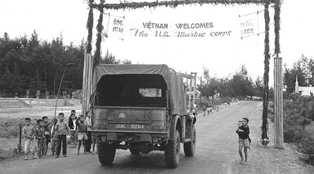 
Chính quyền Sài Gòn đã tổ chức cho các học sinh địa phương chào đón lực lượng viễn chinh đến Đà nẵng - Việt Nam, băng cờ khẩu hiệu dăng trên những tuyến đường hành quân.

Trong hình, cổng chào với khẩu hiệu Chào mừng đến Việt Nam, trẻ em địa phương tò mò và hiếu kỳ nhìn ngắm những xe quân sự Mỹ ở ngoại ô Đà Nẵng. (USMC)
