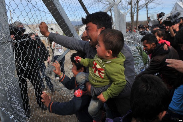 Người đàn ông di cư Afghanistan bế con nhỏ, đẩy hàng rào biên giới với Macedonia tại ngôi làng Idomeni, Hi Lạp.