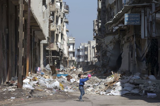 Cậu bé chơi đùa với bóng giữa những tòa nhà bị phá hủy ở thành phố Homs, Syria.