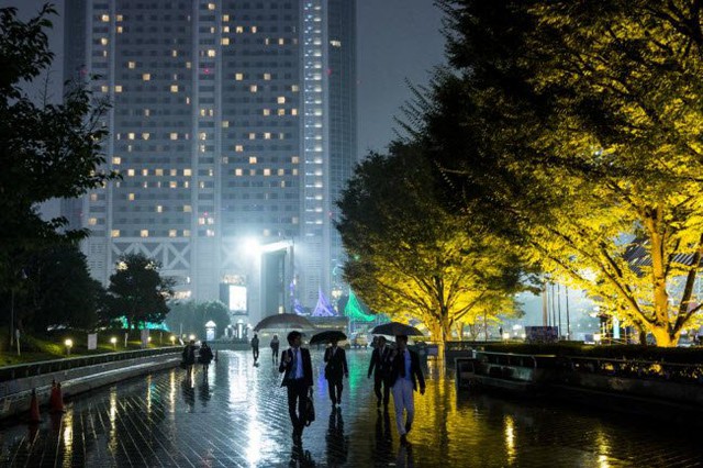 
Mọi người đi dưới trời mưa cạnh hàng cây được chiếu sáng lung linh tại thành phố Tokyo.
