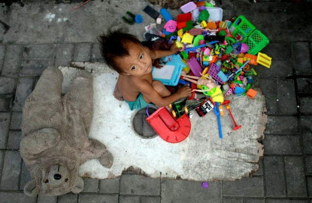 Một cậu bé vô gia cư chơi đùa với những món đồ chơi cha mẹ nhặt được để đem bán ở Manila, Philippines.