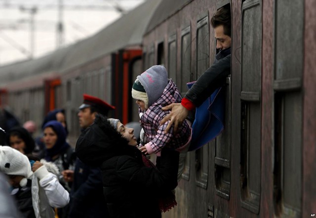Người đàn ông di cư trên tàu đưa đứa trẻ cho người phụ nữ dưới nhà ga tại ngôi làng Tabanovce ở Macedonia.