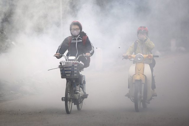 Mọi người đi xe qua khói bốc lên từ đống rác được đốt ven đường tại Hà Nội, Việt Nam.