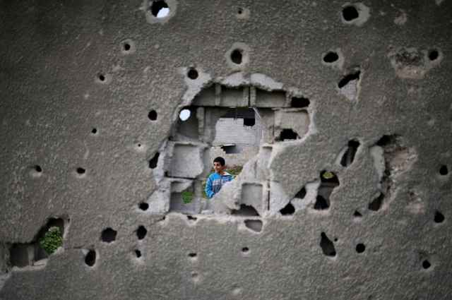 Cậu bé Palestine phía sau bức tường chi chít vết đạn của tòa nhà đã bị phá hủy trong cuộc chiến 50 ngày giữa Israel và các chiến binh Hamas trong mùa hè năm 2014, tại thành phố Gaza.