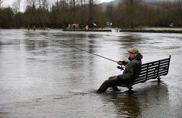 Người đàn ông ngồi trên ghế, câu cá trong dòng nước lũ ở Stirling, Scotland.