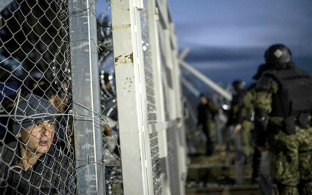 Cảnh sát Macedonia đứng bảo vệ dọc hàng rào biên giới khi người di cư nhìn qua hàng rào từ ngôi làng Gevgelija, Hi Lạp.
