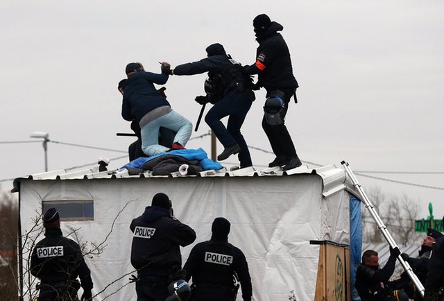 Cảnh sát khống chế một người phụ nữ cầm dao đang đe dọa sẽ tự cắt cổ tay khi khu trại tị nạn “Jungle” ở Calais, Pháp, bị dỡ bỏ.