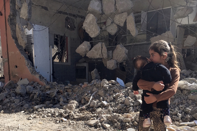 Bé gái bế em nhỏ trước tòa nhà đổ nát tại thành phố Cizre, Thổ Nhĩ Kỳ.
