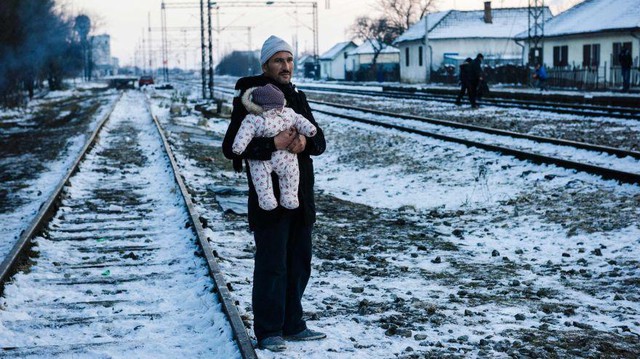 Một người đàn ông bế con đứng chờ những người tị nạn khách tại một ga xe lửa tại thị trấn Presevo, miền nam Serbia.