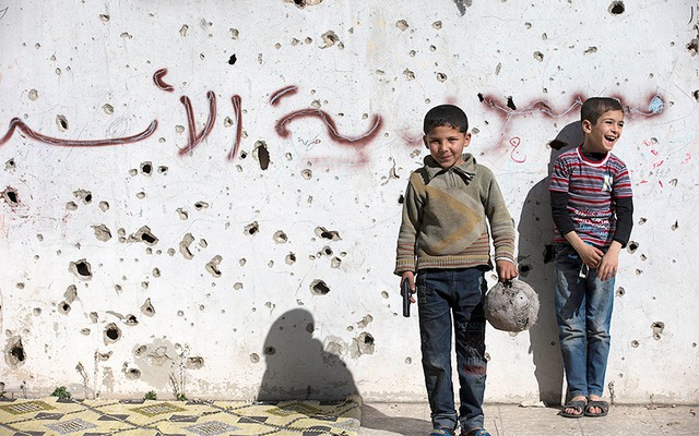 
Cậu bé cầm súng đồ chơi trong khi chơi đá bóng với những đứa trẻ giữa tòa nhà đổ nát ở thành phố Homs, Syria.
