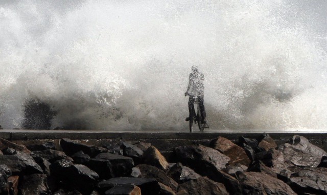 
Một người đàn ông bị sóng vùi dập khi đạp xe qua cảng cá Chennai, Ấn Độ ngày 28/12/2011
