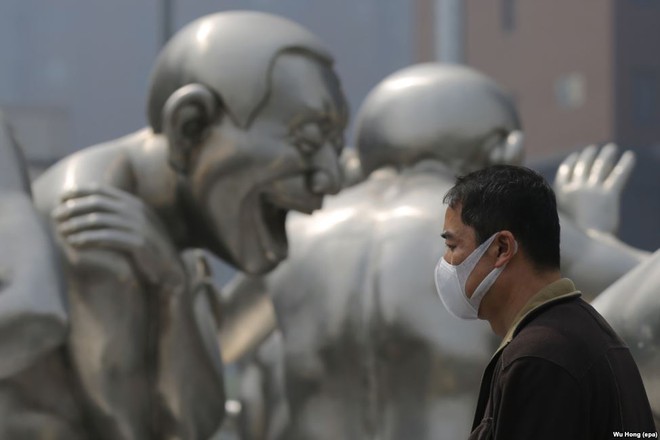 Người đàn ông đeo khẩu trang đi qua bức tượng lớn trong một ngày nhiều sương mù ở Bắc Kinh, Trung Quốc.