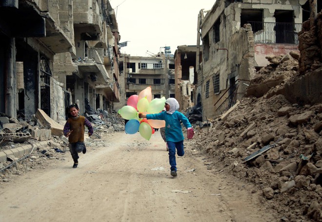 Trẻ em cầm bóng bay chạy qua những tòa nhà đổ nát tại thị trấn Jobar ở ngoại ô thủ đô Damascus, Syria.