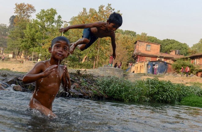 Các bé trai nô đùa trên một con sông để tránh cái nóng ở Kathmandu, Nepal.
