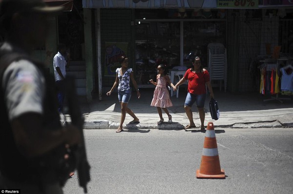 Cảnh sát cầm súng trường tuần tra khi một gia đình đi qua đường phố tại khu ổ chuột Nordeste de Amaralina.