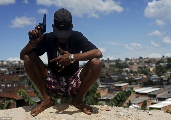 Một thành viên của băng nhóm tội phạm cầm súng ngồi trên đỉnh đồi nhìn xuống một khu ổ chuột ở Salvador.