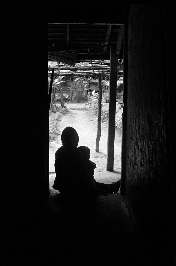 Một phụ nữ và em bé Việt Nam ngồi trước cửa nhà.