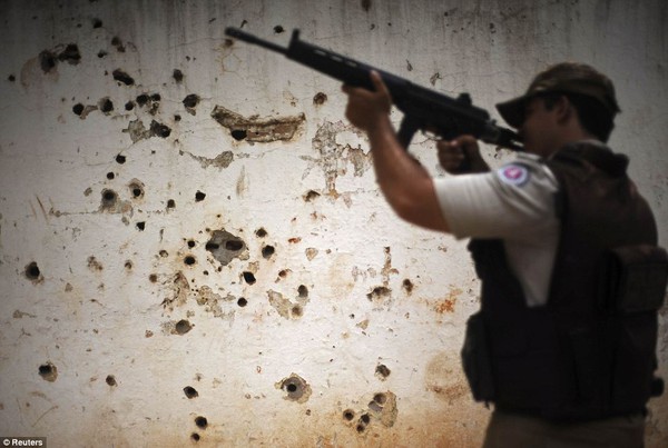 Cảnh sát đi tuần tra qua bức tường đầy vết đạn bắn sau các cuộc đấu súng giữa băng nhóm tội phạm tại khu ổ chuột Nordeste de Amaralina.