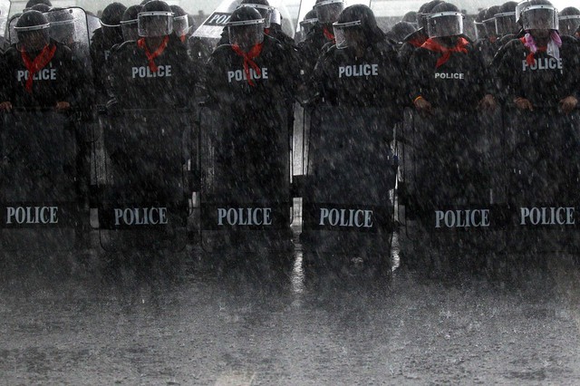 Cảnh sát chống bạo động đứng dưới mưa lớn để ngăn chặn nông dân biểu tình gần một sân bay ở Surat Thani, Thái Lan.