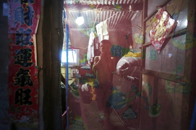 Một cậu bé nhìn ra ngoài từ sau màn cửa nhà tại một khu ổ chuột gần đường vành đai số 2 quanh thành phố Bắc Kinh, Trung Quốc.