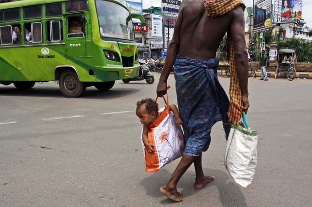 Một người đàn ông xách con trong túi đi qua đường phố ở Bhubaneswar, Ấn Độ.